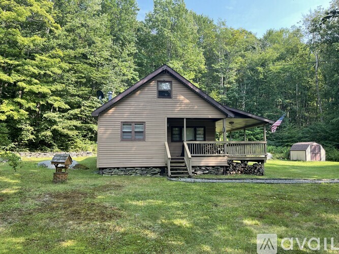 A small wooden cabin with a porch and a flag on it is surrounded by trees.