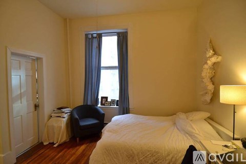 A bedroom with a bed, chair, and window.