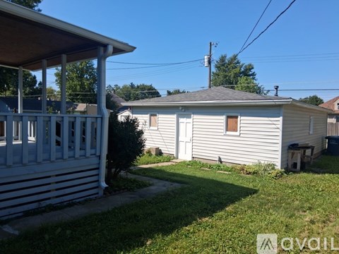 A house with a white siding and a brown door is surrounded by a grassy area.