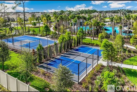A tennis court surrounded by trees and a pool.