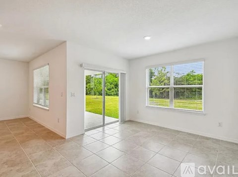 A spacious room with tiled flooring and sliding glass doors leading to a green outdoor area.