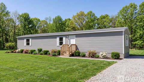 A grey house with a white door and windows is surrounded by greenery.