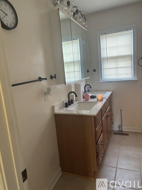 A bathroom with a sink, mirror, and a window with blinds.