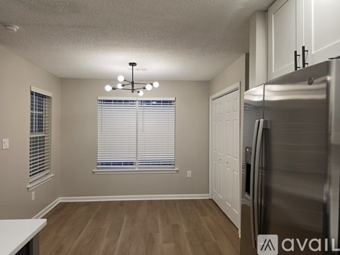 A kitchen with a refrigerator, cabinets, and a window with blinds.
