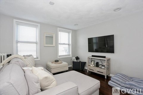 A living room with a white couch and a flat screen TV mounted on the wall.