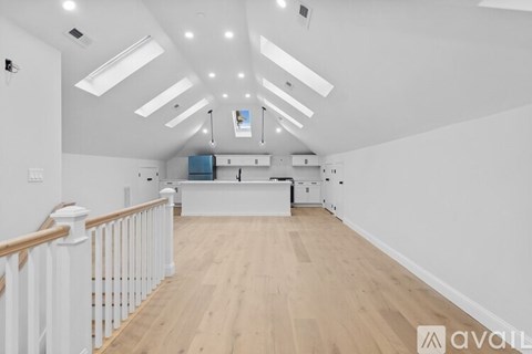 A spacious room with wooden floors and white walls, featuring a kitchen area with white cabinets and appliances.