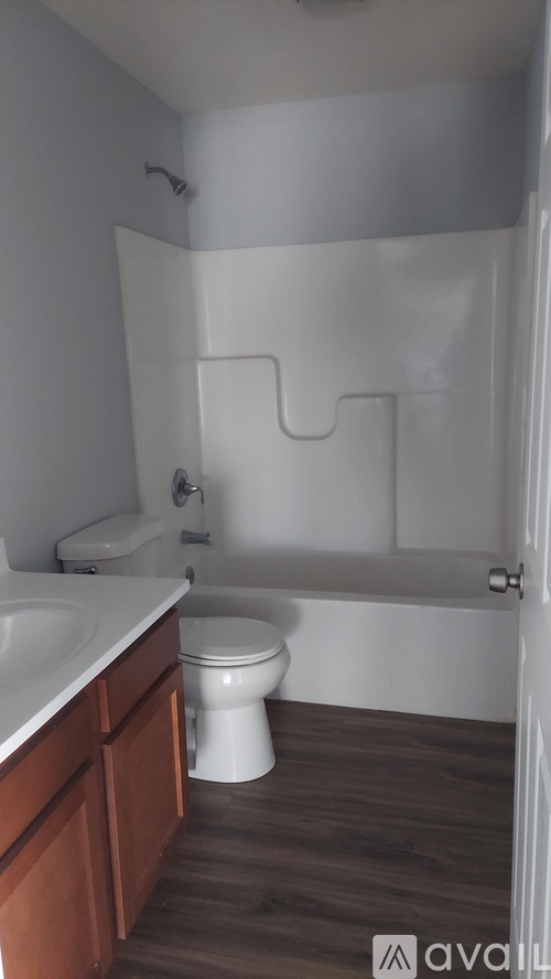 A white toilet sits in a bathroom with wooden floors and white walls.