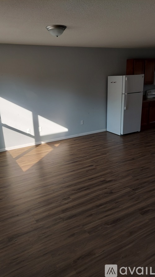 A white fridge in a room with wooden floors and a window.