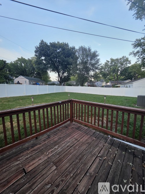 A wooden deck with a railing and a view of a white fence and trees.