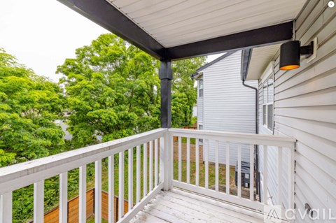 A balcony with white railings and a view of a green tree.