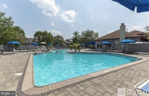 A large outdoor swimming pool surrounded by a stone patio and blue umbrellas.