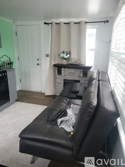 A black leather couch in a living room with a fireplace and a green wall.