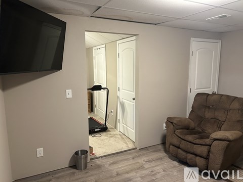 A room with a brown recliner chair, a flat screen TV, and a vacuum cleaner.