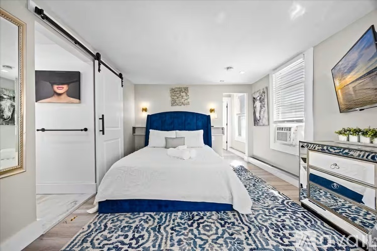 A bedroom with a white bed and blue patterned carpet.