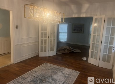 A room with a chandelier, a rug, and a coat on the floor.