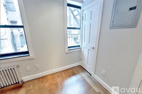 A room with a white door, a window with a view of a city, and a radiator on the floor.
