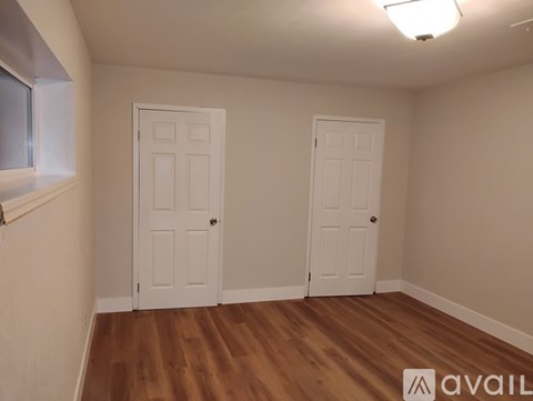 Two white doors in a room with wooden floors and white walls.