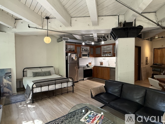 A bedroom with a bed, couch, and a kitchen area in the background.
