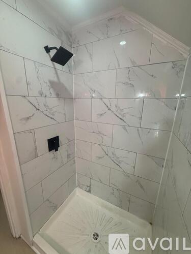 A white marble tiled shower with a black faucet.