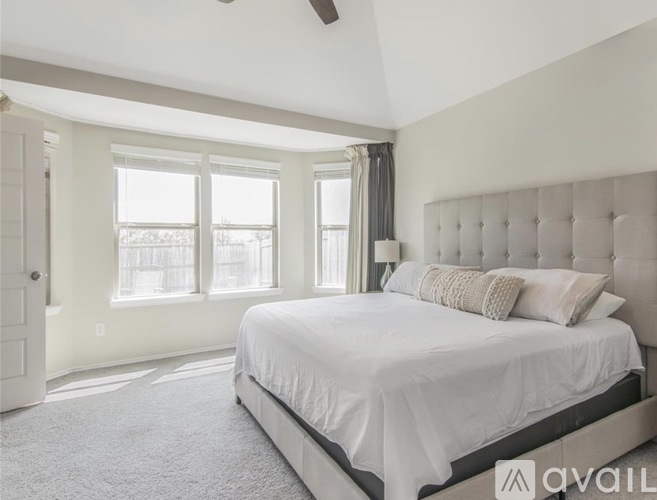 A bedroom with a large bed and a window with curtains.