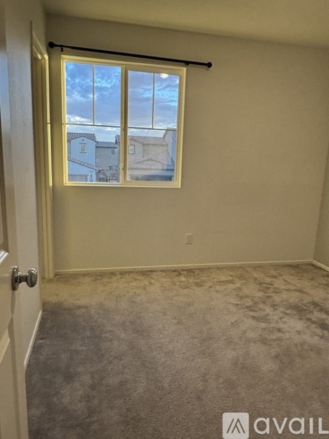 A room with a carpeted floor, a window with a view of buildings outside, and a door leading to another room.