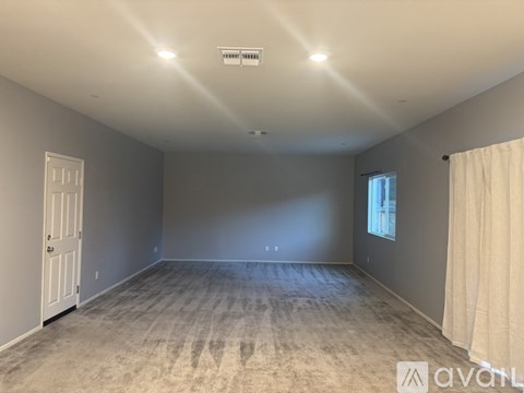 A spacious room with a carpeted floor and a window with curtains.