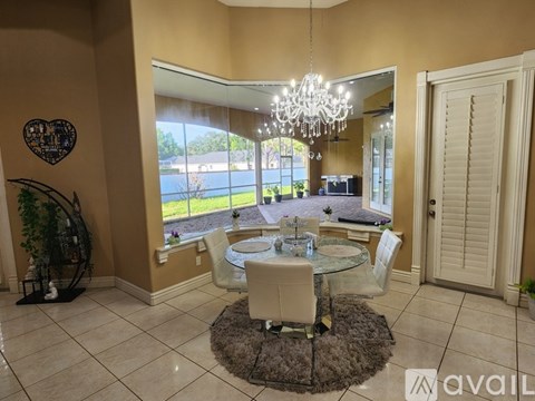 A dining room with a glass table and chairs, a chandelier, and a view of the outdoors through the window.