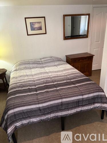 A bed with a striped comforter is in a room with a mirror and a picture on the wall.