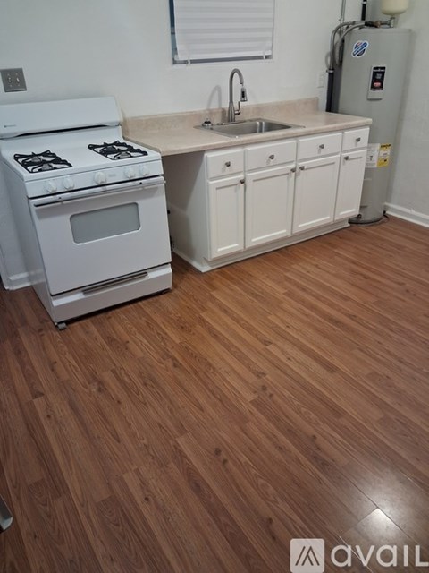A kitchen with a white stove and white cabinets with a wooden floor.