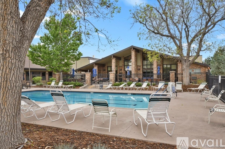 A pool surrounded by chairs and trees with a building in the background.