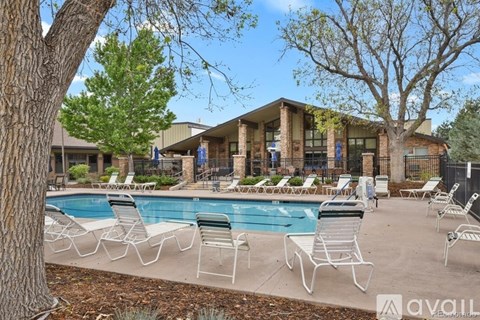 A pool surrounded by chairs and trees with a building in the background.