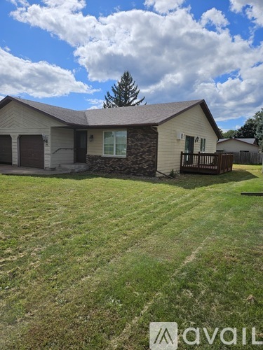 A house with a brown roof and a stone wall is surrounded by a grassy lawn.