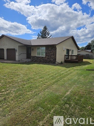 A house with a brown roof and a stone wall is surrounded by a grassy lawn.