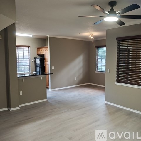 A room with a ceiling fan and light, a window with blinds, and a wall with a light switch.