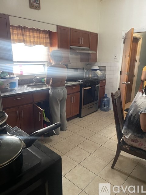 A woman is standing in a kitchen with wooden cabinets and a black stove.
