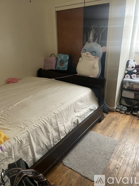 A bedroom with a bed, a grey rug, a backpack and a wall with a picture of a cat.