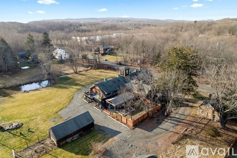 A bird's eye view of a house surrounded by trees and a pond.