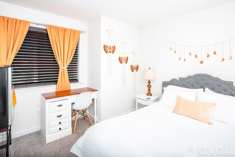 A bedroom with a bed, desk, and orange curtains.