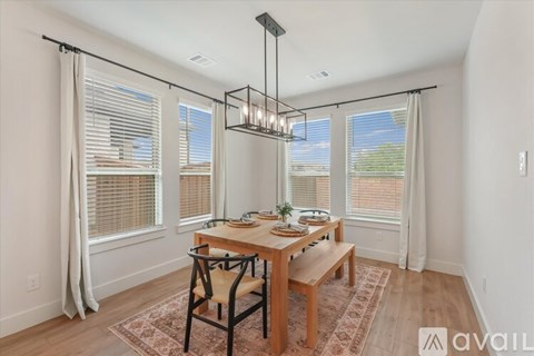 A dining room with a wooden table and chairs, a chandelier, and a view of the outdoors through the windows.