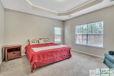 A bedroom with a red bedspread and a window with blinds.