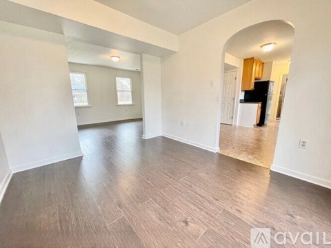 A spacious room with wood flooring and a large archway leading to another room.
