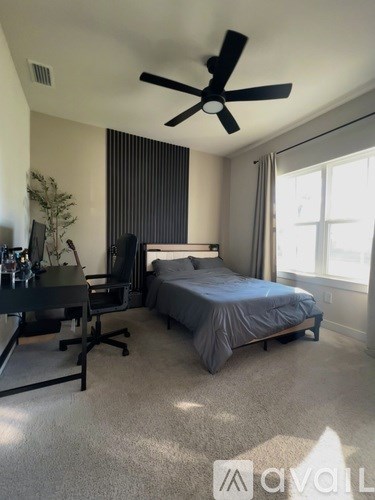 A bedroom with a bed, desk, and ceiling fan.