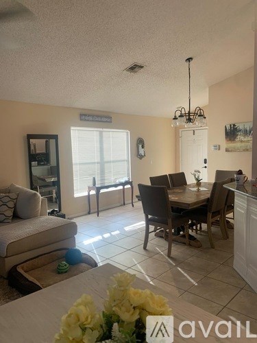A dining room with a table set for four and a couch with a pillow and a vase of flowers on it.