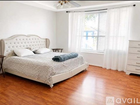 A bedroom with a large bed and a window with white curtains.