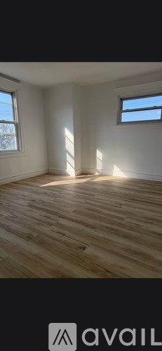 A room with wooden flooring and two windows letting in sunlight.