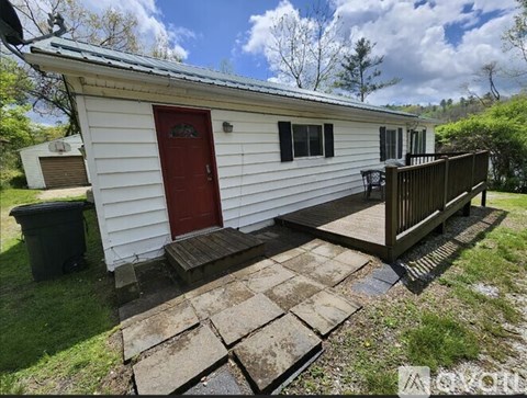 A small white house with a red door and a wooden deck.