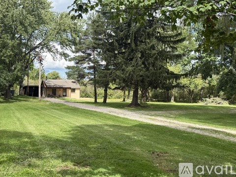 A house is surrounded by trees in a grassy area.
