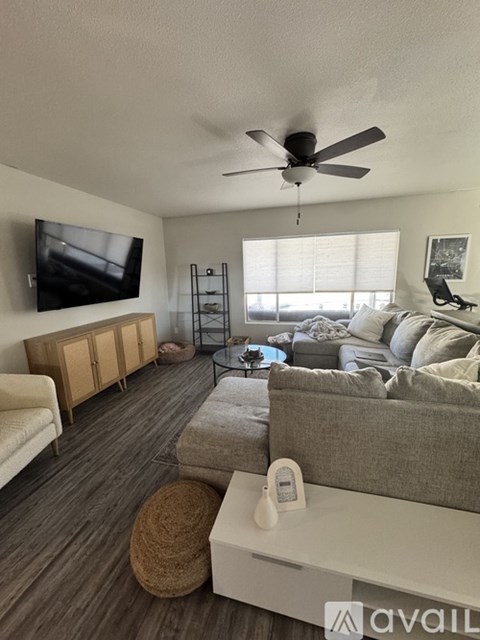 A living room with a grey couch, a white coffee table, and a flat screen TV mounted on the wall.
