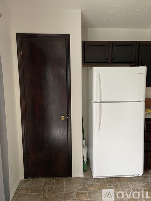 A white refrigerator is in a kitchen next to a brown door.