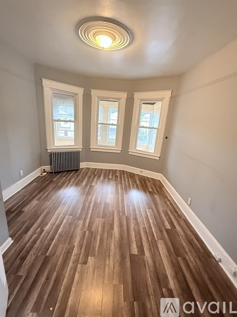 A room with wooden flooring and two windows.